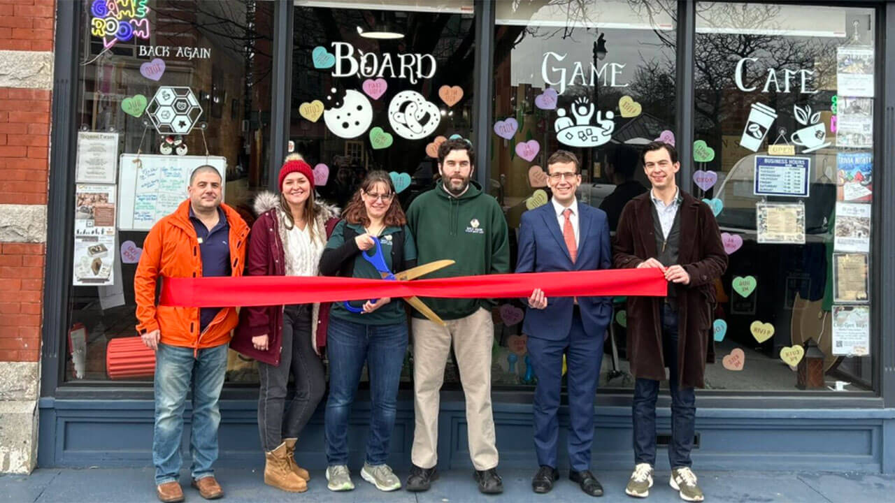 A group of people stand in front of a store with a large ribbon and scissors.