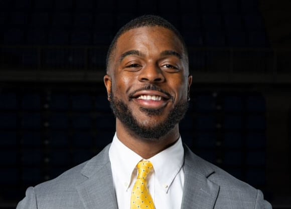 Aaron Robinson smiles for a headshot wearing a suit and a yellow tie.