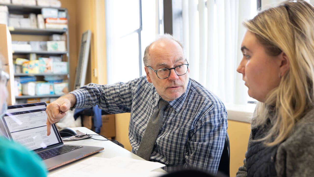 Professor Matthew Maron shows a student how to file taxes online pointing to a computer.