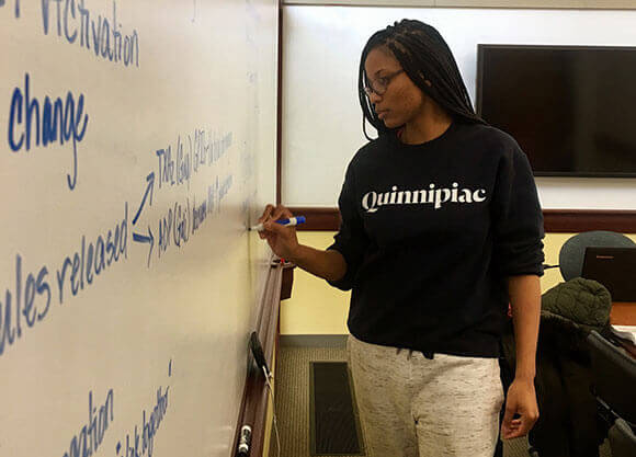 Tiana Clemons, MS '19, writes on a marker board.