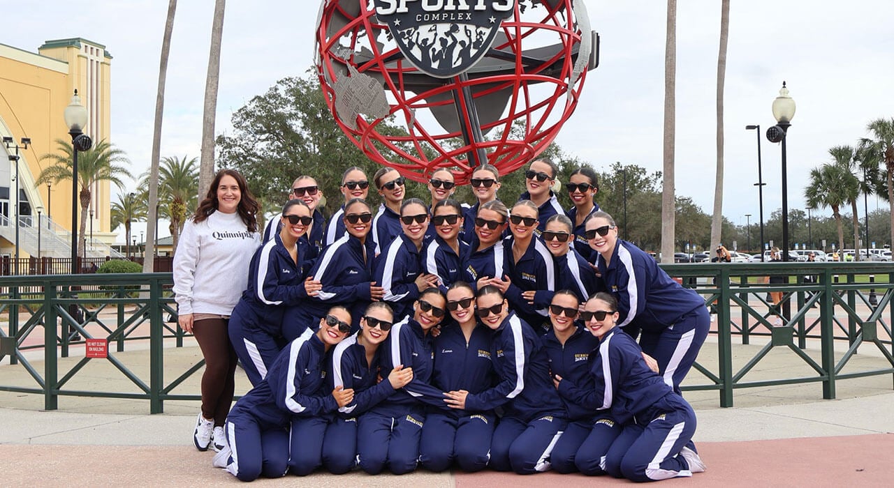 dance team poses with their coach in front of the sports complex sign