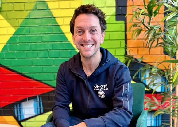 Scott Wormers smiles in his work uniform with a colorful background.