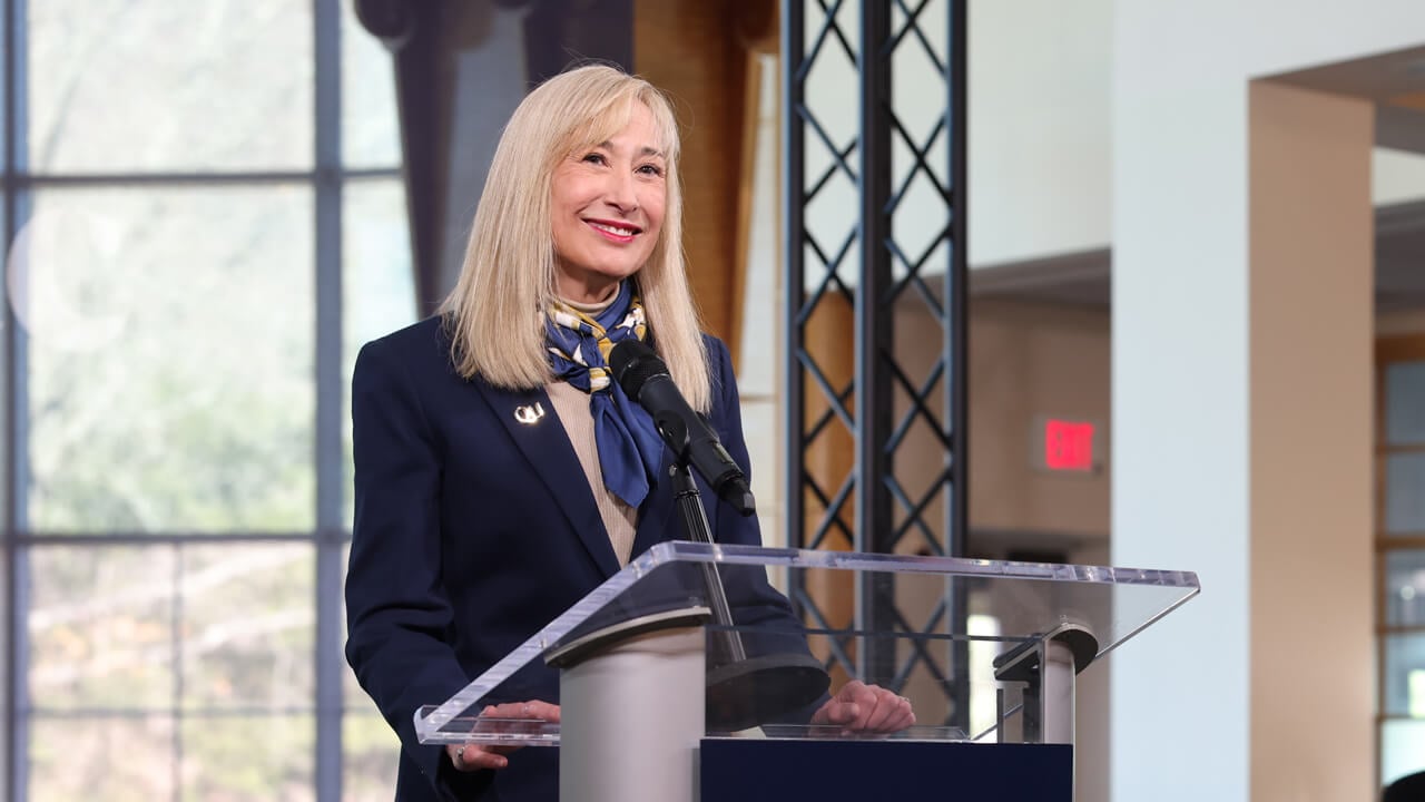 Marie Hardin smiles as she stands behind a podium in the Quinnipiac open air studio