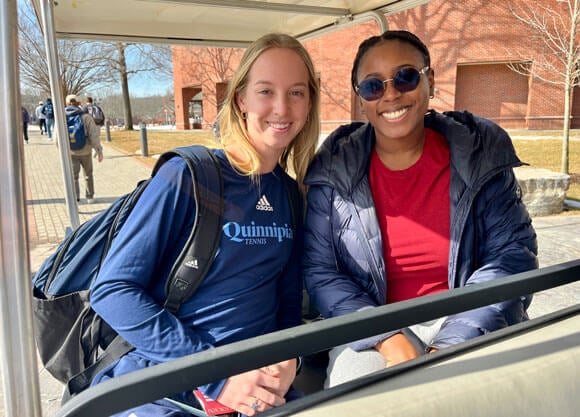 Two people are sitting in a golf cart on Quinnipiac's Mount Carmel Campus