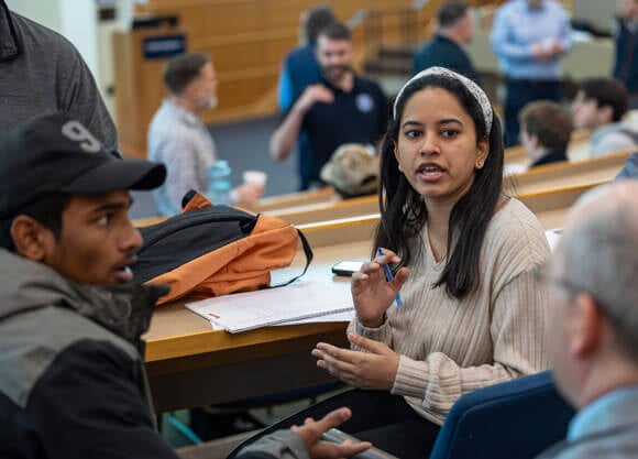 A student speaks to others in the Mount Carmel Auditorium, holding a pen in their hand.