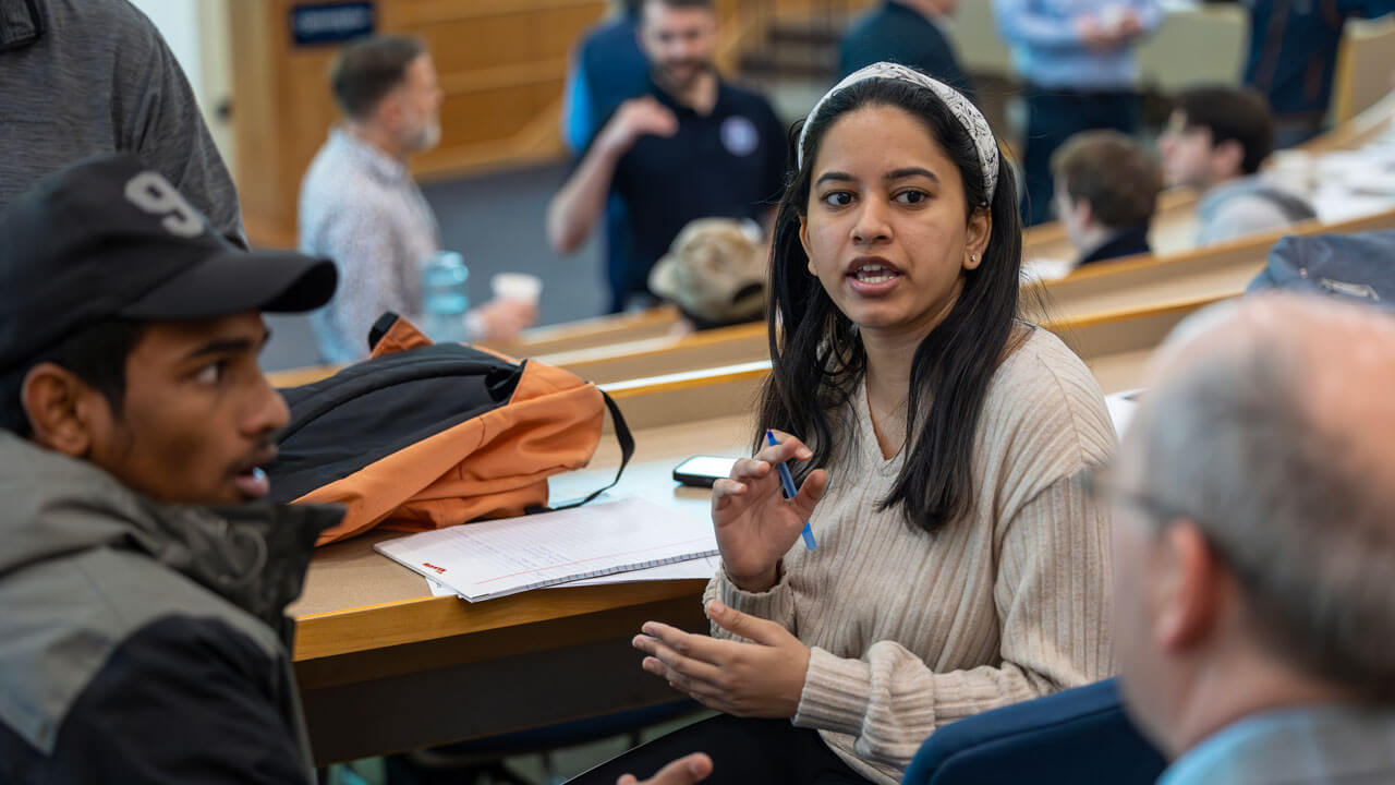 A student holds a pen in her hand, talking to others in the Mount Carmel Auditorium.