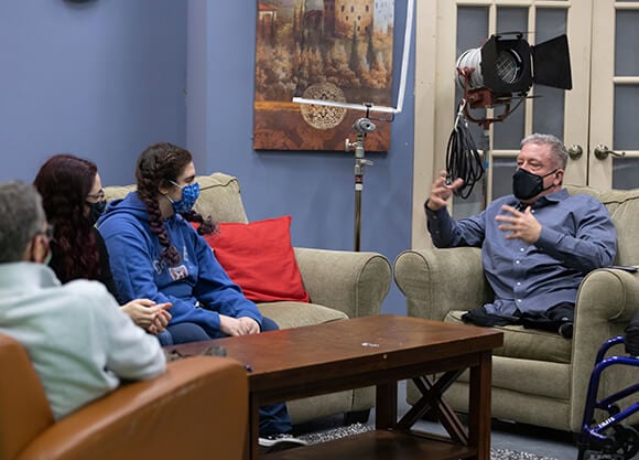 Dave Stevens speaks to 2 students sitting on a couch.