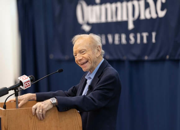 Joseph Liberman standing at a podium speaking to Quinnipiac students