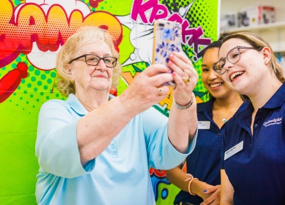 Two OT students teach an older adult how to take a selfie using a cell phone