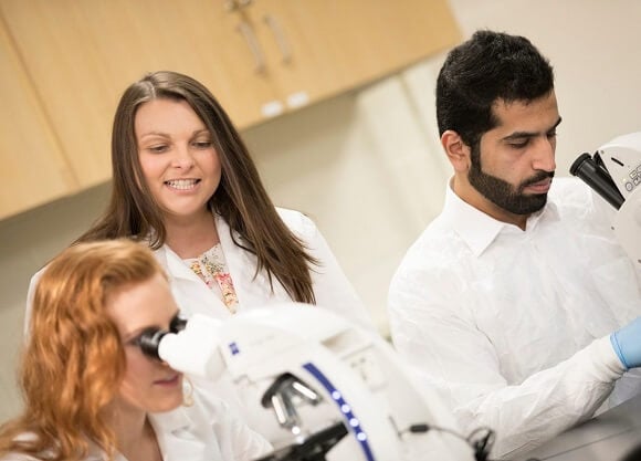 Students work on a microscope as Professor Mirrione looks on.