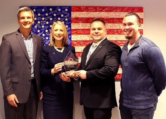 Four people stand holding the glass award.