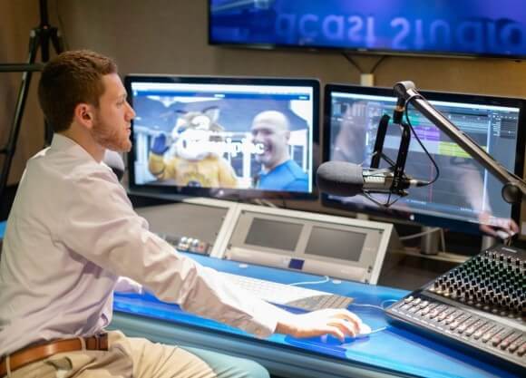 Kevin Meiselman sits in front of computer set up in the Podcast Studio