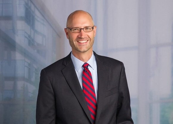 Headshot photograph of Daryl Richard smiling, wearing a suit and red and blue striped tie