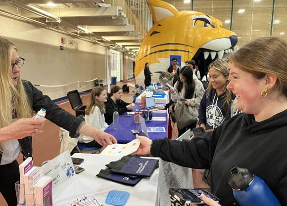 A student smiles while being handed a paper in front of the large blowup Bobcat.