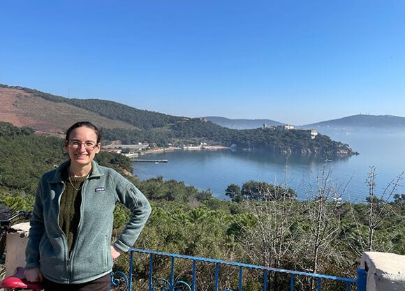 Student standing on a mountaintop in front of a backdrop of mountains and water.