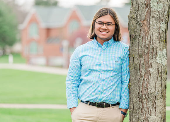 Sean Formantes smiles against a tree in a blue shirt.