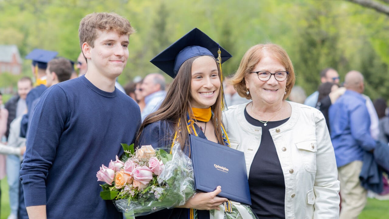 Graduate smiles with her family while holding up her diploma and a bouquet of flowers