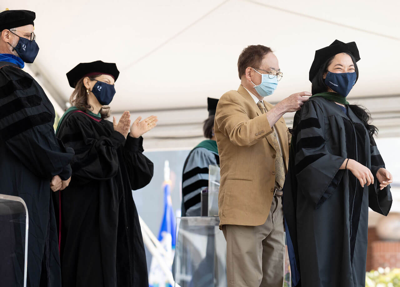 A graduate receives her doctoral hood from her father during Commencement