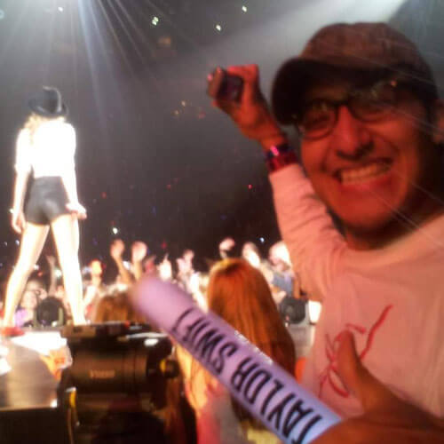 Professor Ari Perez at a Taylor Swift concert smiling with Taylor Swift in the background