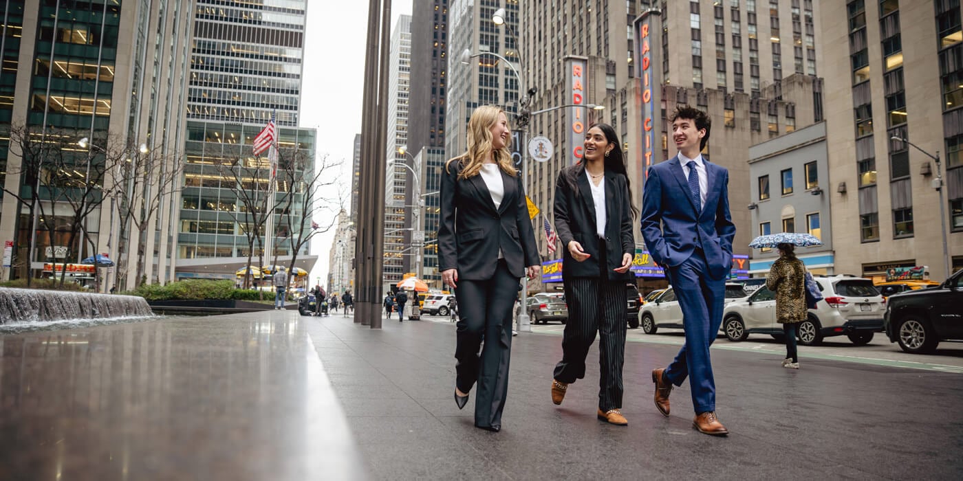 A group of three students walk down the street in professional attire.