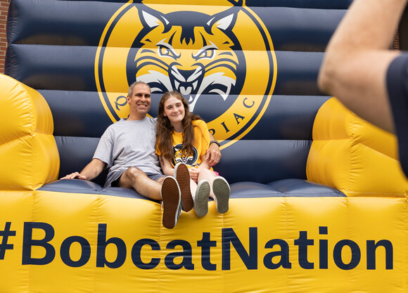 A new student and father pose for a photo on a giant inflatable couch that reads Bobcat Nation