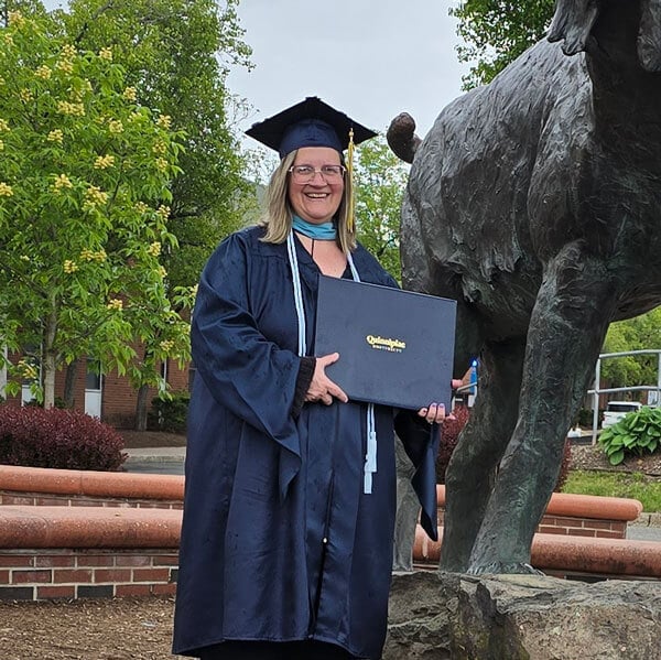 Michele Marchetti holding her degree in her cap and gown