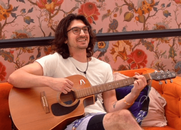 John Franklin playing guitar on a bright orange couch.