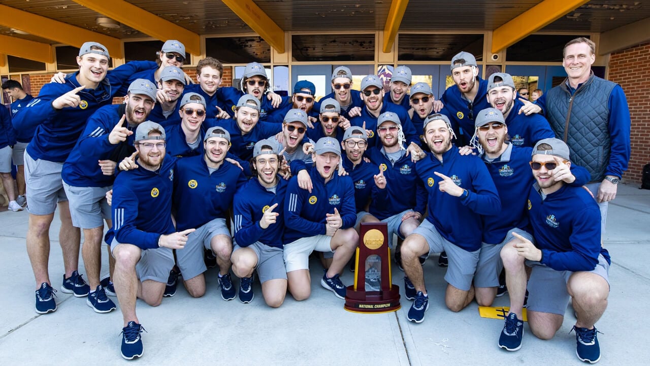 Men's ice hockey team members and coach pose and cheer with the national champions trophy