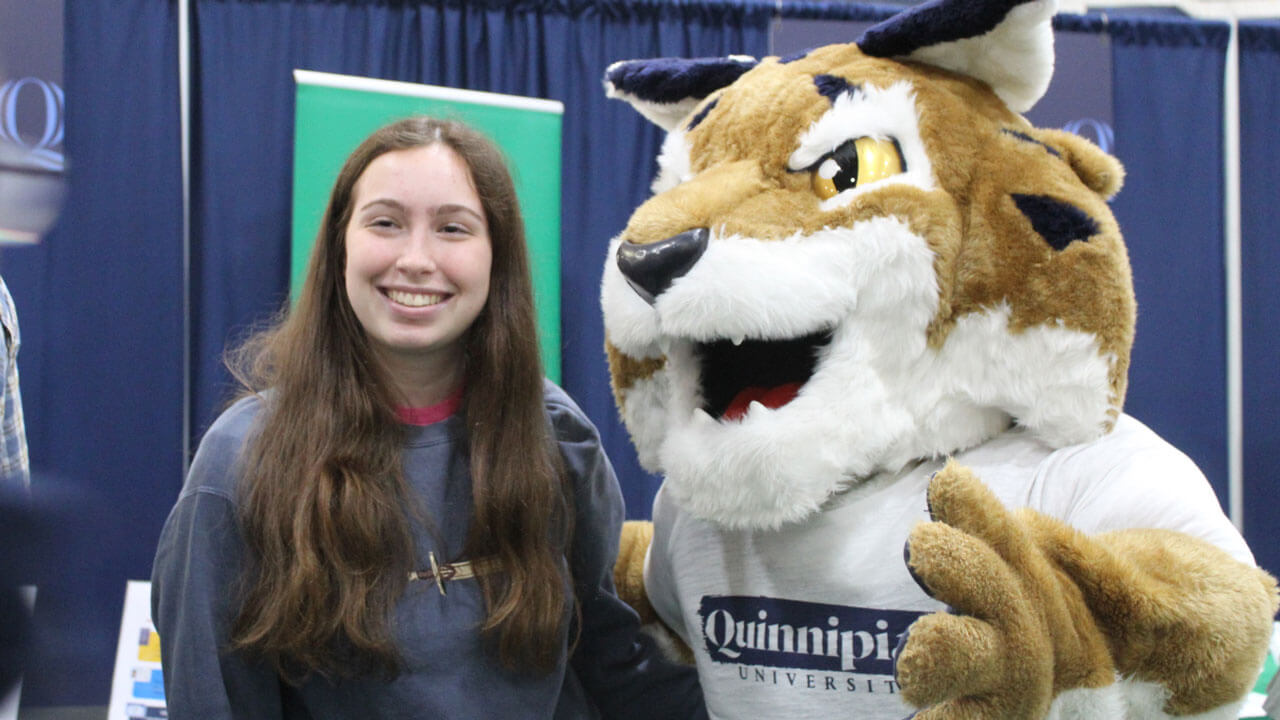 Boomer wearing a Quinnipiac shirt and taking a photo with a student