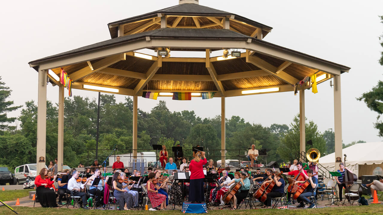 An orchestra plays in front of the Hamden town gazebo while a conductor in red waves her baton