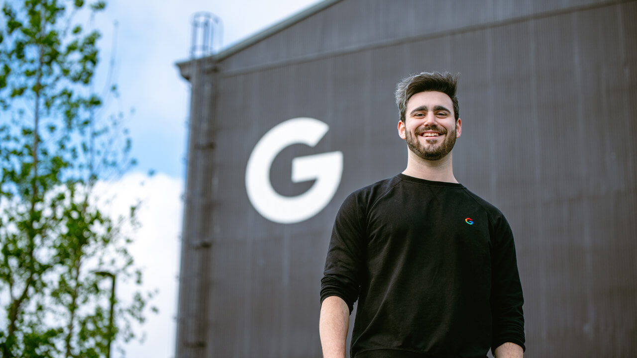 Sam poses for a photo in front a building with a large Google G logo