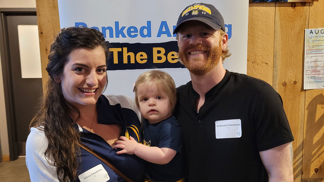 Two alumni take a photo with their baby at an alumni event