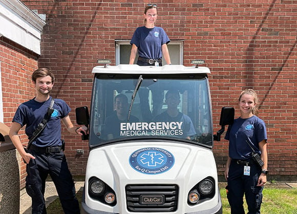 QU EMS Members, Charles Dunn, Vanessa Infante and Heidi Reinemann standing outside of their Club Car.