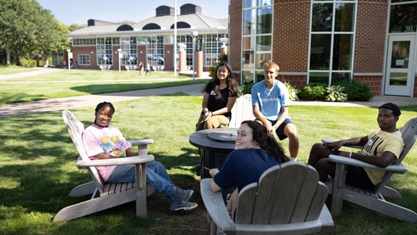 A group of friends chilling on the Adirondack chairs outside the Carl Hansen Student Center