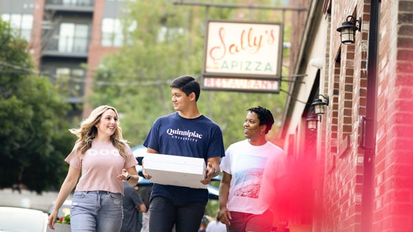 Students walking through New Haven smiling while holding a pizza box