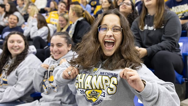 Students in National Champions gear cheer enthusiastically for the men's ice hockey team