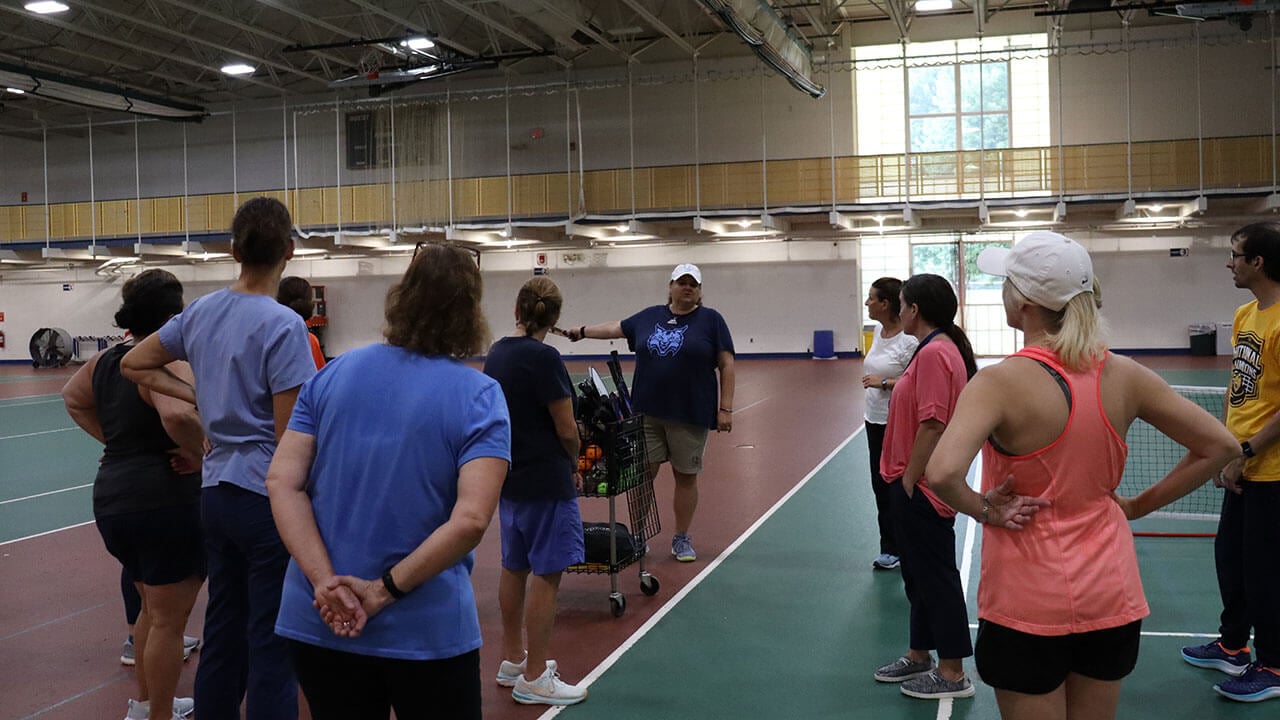 Quinnipiac faculty come together as a group to learn the basics of pickleball at the gym.