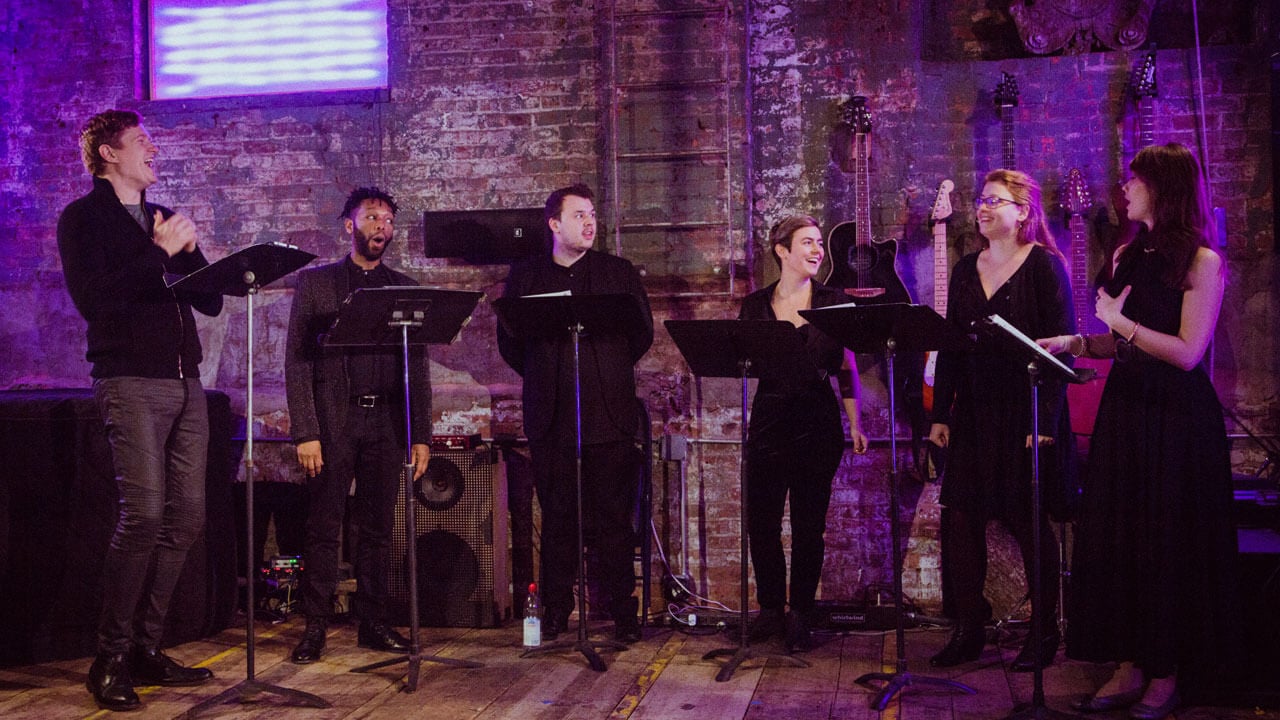 The 6 members of The New Consort singing in front of music stands