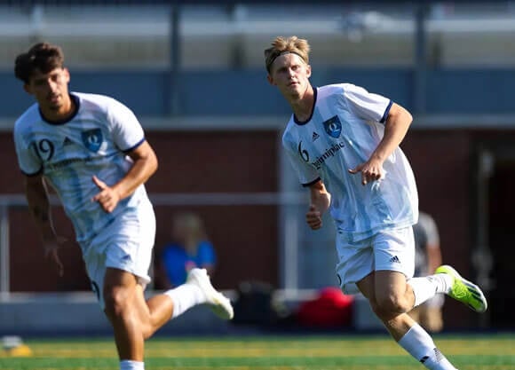 Two Quinnipiac mens's soccer players look to right while running up the field