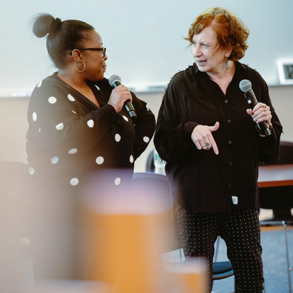 Cindy Maher and Carol Grannis hold microphones and speak in Quinnipiac's Mount Carmel Auditorium