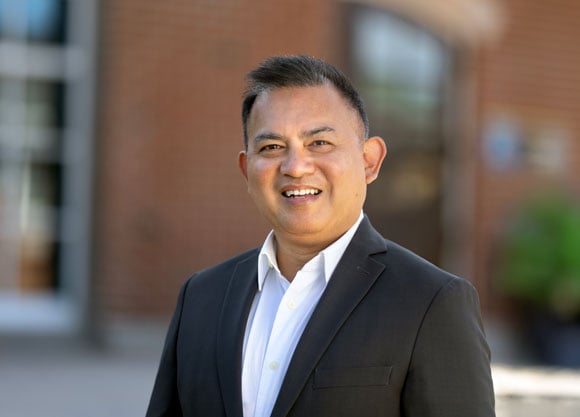 Headshot of librarian Robert Joven in front of the Arnold Bernhard Library.