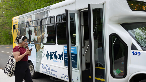 A student wearing headphones and looking at her mobile approaches a Quinnipiac shuttle to board