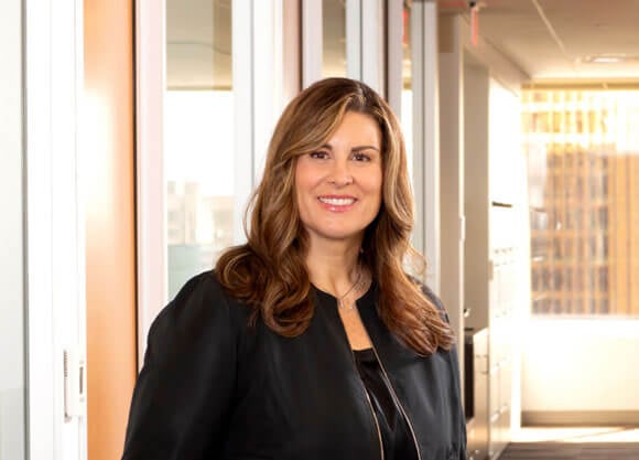 Jeanna Doherty standing and smiling for a headshot.