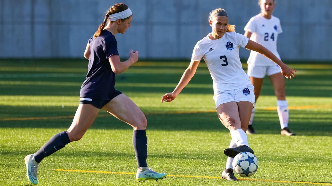 Quinnipiac women's club soccer players kick around a ball on the field.