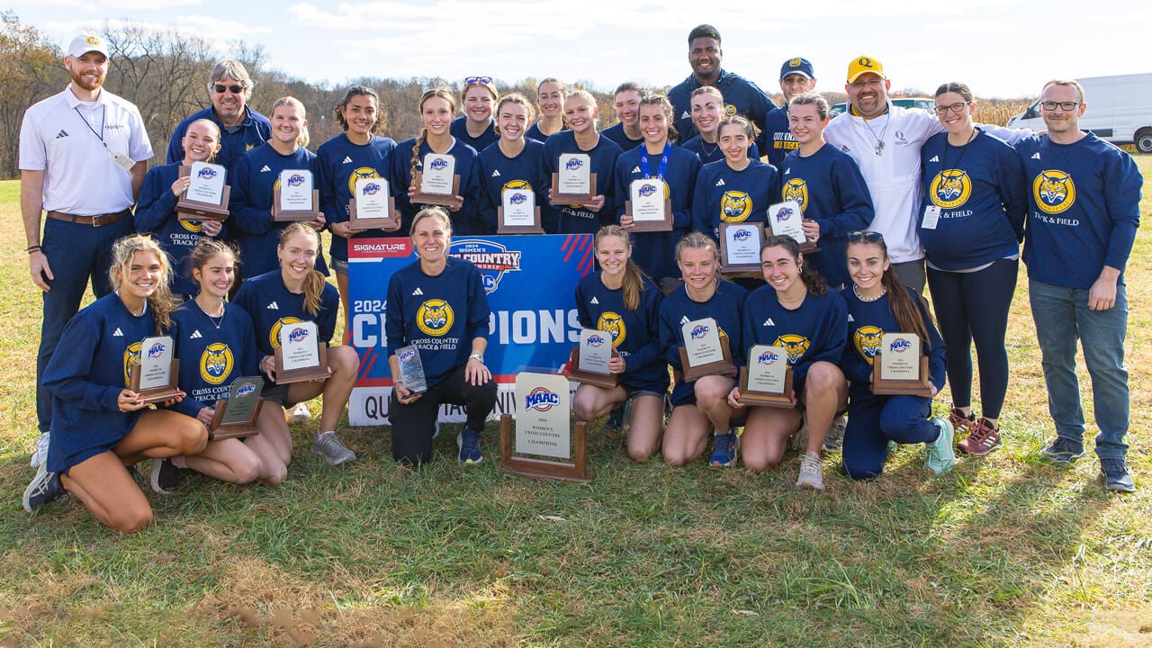 Quinnipiac women's cross country team, coaches and staff pose with MAAC champions signs and trophies