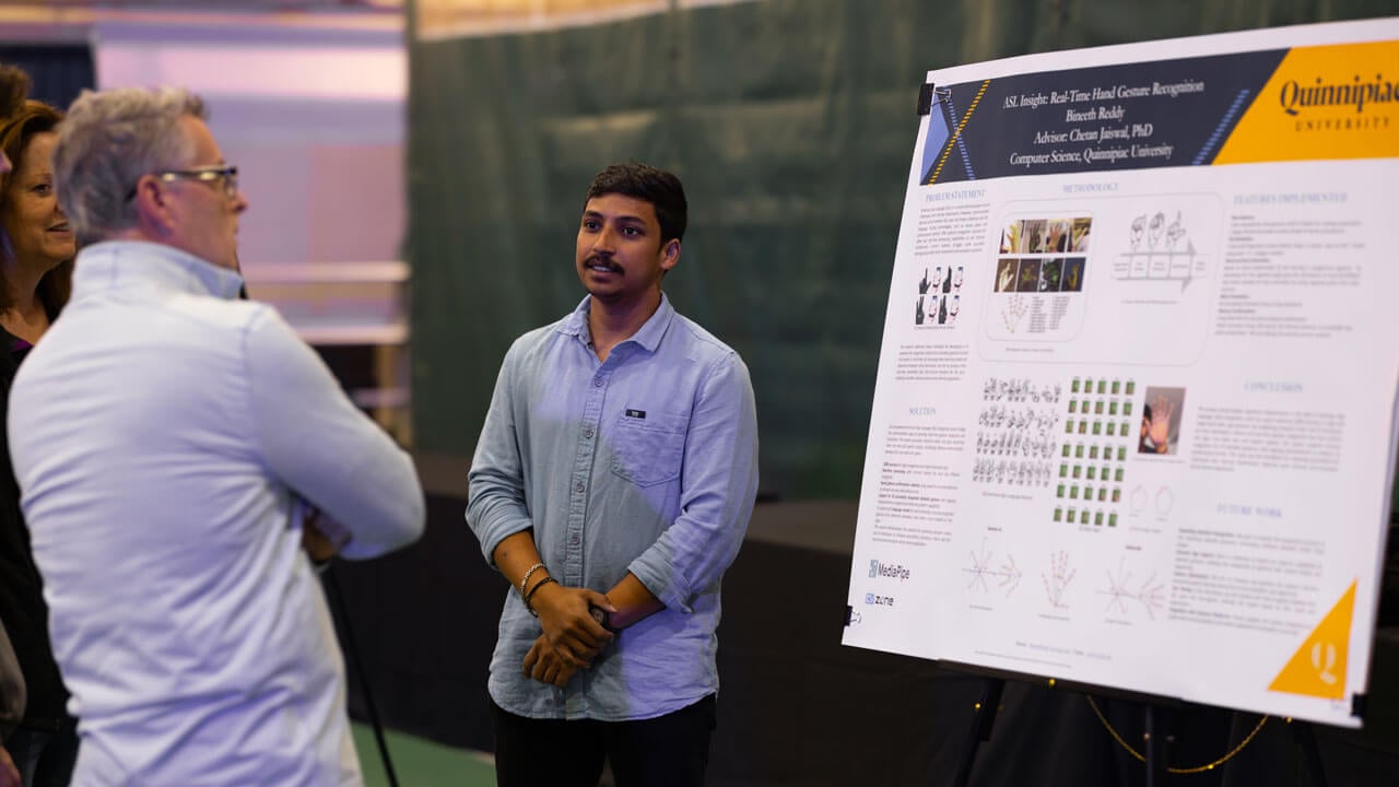 Student stands alongside his research board while spectators view his research