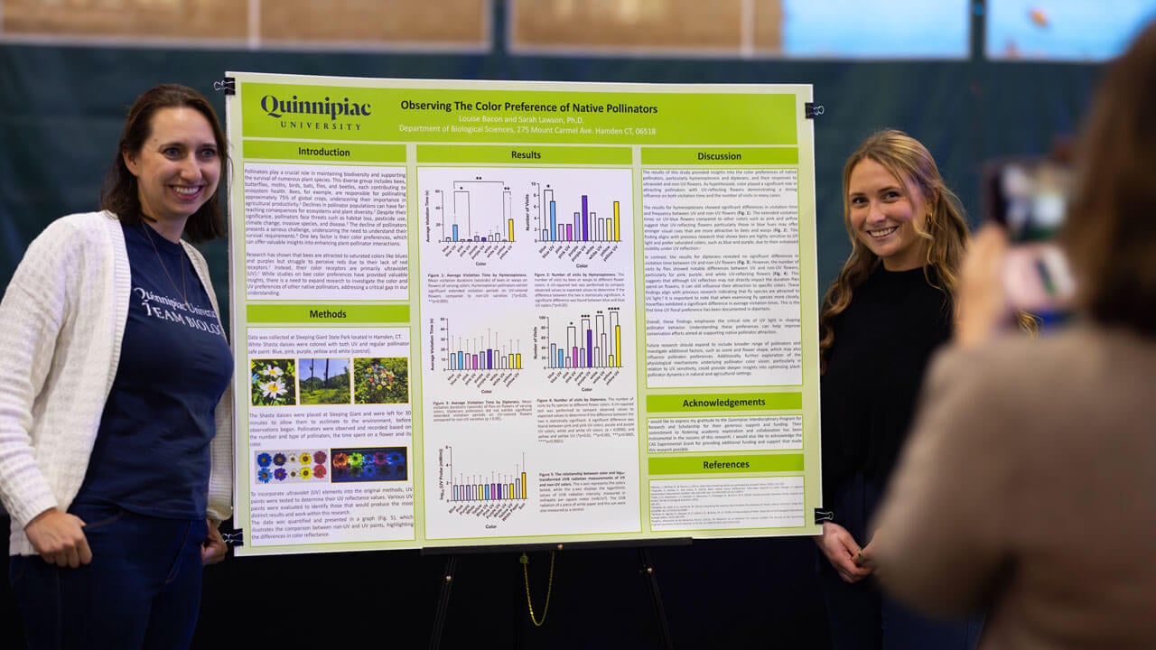 A professor smiles alongside a student in front of her research presentation