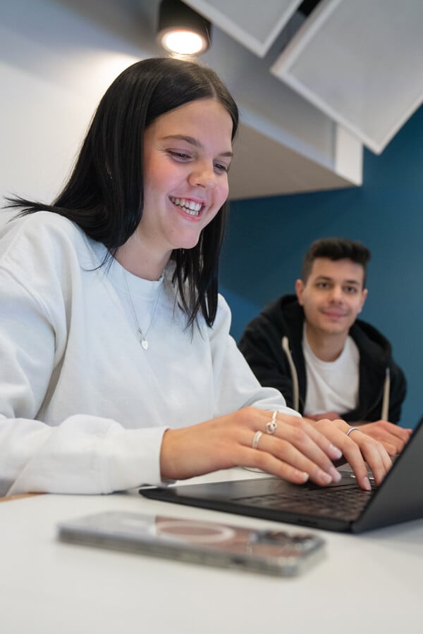 A female student working on a laptop with a male student in the background