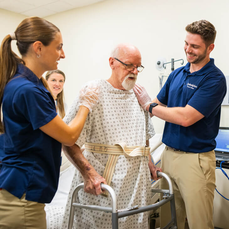 Health science students help their patient stand up to his walker.