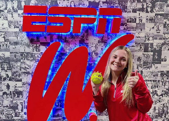 Lo Yarnall holding a softball and smiling in front of an ESPN W sign